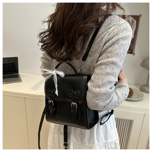 Detail of a black PU leather backpack with lace bows shown on model in a soft room