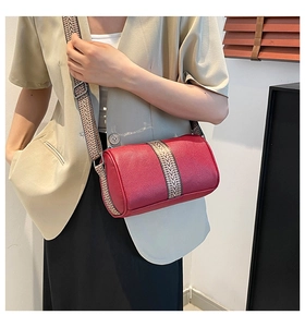 Close-up of red cylindrical crossbody bag with wide black and white geometric strap