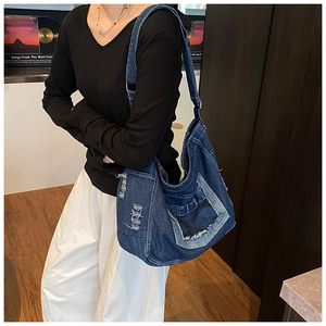 Detail of a large blue washed denim messenger bag featuring fringe and vintage distressing