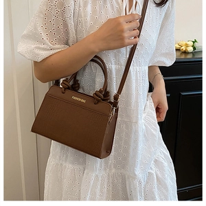 Detail of a brown crocodile pattern saddle bag with a stylish knot handle and long strap