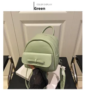 Detail of a mini green leather backpack featuring a matching bow and adjustable straps