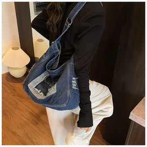 Dettaglio di una borsa tote in denim blu con finiture usurate e cuciture a contrasto
