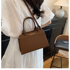 Detailed view of brown crocodile-embossed leather handbag with gold logo and dual handles