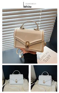 Détail du petit sac blanc avec fermoir rotatif doré et poignée supérieure élégante