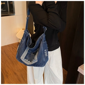 Detail of dark blue denim crossbody bag with frayed edges and adjustable wide strap