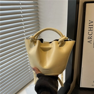 Elegant cream bucket bag with unique knot handle design and adjustable shoulder strap