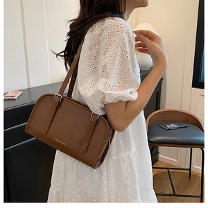 Brown leather crossbody bag with adjustable straps and gold logo on white lace dress