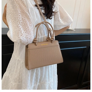 Detail of khaki crocodile pattern handbag with gold fashion bag logo and knotted handle