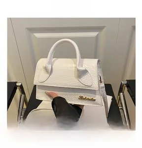 Detailed macro of white crocodile-embossed leather handbag with gold metal logo hardware