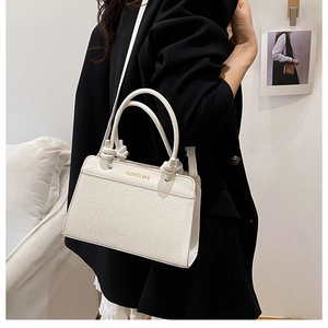 Detail of white crocodile pattern shoulder bag with decorative knotted handles and gold text