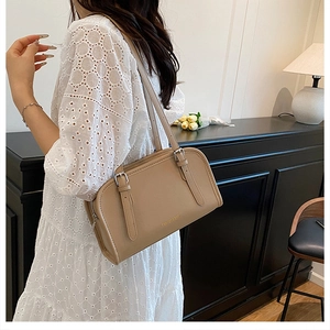 Close-up of khaki leather underarm bag with adjustable strap on a white lace dress
