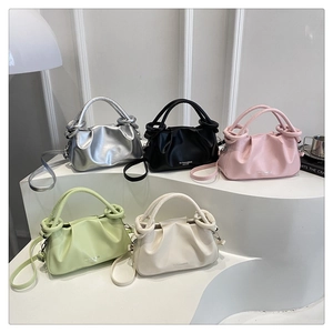 Detail of five stylish pleated cloud bags in silver black pink green and beige on a white stand