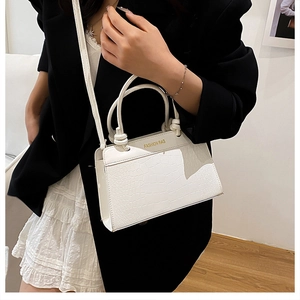 Detail of white crocodile embossed tote bag shown on model in indoor minimalist setting