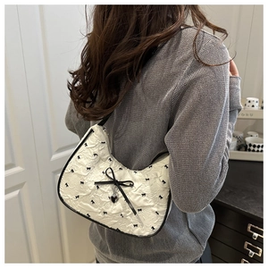 Close-up of a white baguette bag featuring black bow patterns and silver heart charm