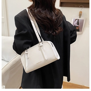 Model wearing a minimalist cream Boston handbag with adjustable straps in a studio setting