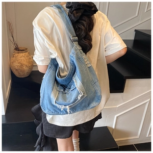 Denim shoulder bag with vintage distressed details and fringe shown in a lifestyle setting