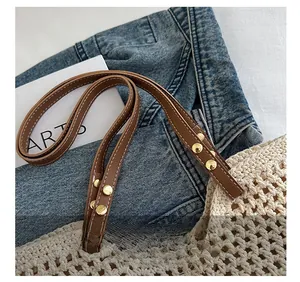 Dettaglio della tracolla in pelle marrone con rivetti dorati su borsa tote in beige