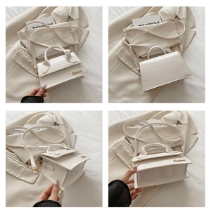 Detail of white crocodile texture mini handbag with gold metal lettering and shoulder strap