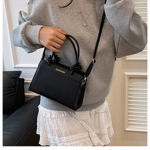 Close-up of black crocodile pattern faux leather handbag with golden hardware and fashion text