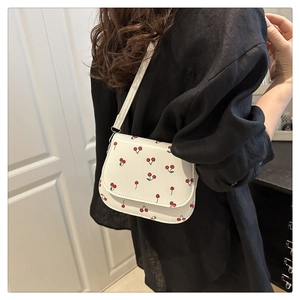 Close-up of white crossbody bag with cherry prints on black clothing background