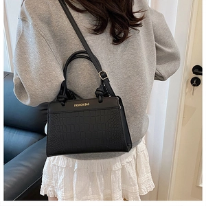 Close-up of black crocodile pattern saddle bag worn with casual grey sweatshirt and white skirt