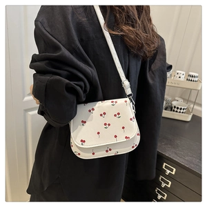 Detail of white leather shoulder bag with red cherry print and adjustable strap