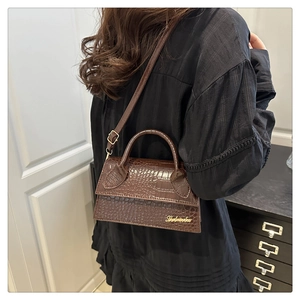 Detailed view of dark brown croc-effect shoulder bag with gold letter logo and strap
