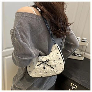 Close-up of white embossed underarm bag with black bow prints and metal heart pendant