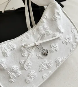 Primer plano de bolso blanco con textura floral, lazo y colgante de corazón.