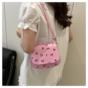 Detail of pink PU shoulder bag with cherry print and adjustable strap on model
