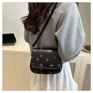 Detail of a black leather mini bag with red cherry prints and adjustable shoulder strap
