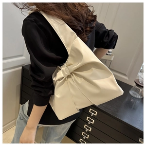 Close-up of creamy white tote bag with bow design on shoulder of a model