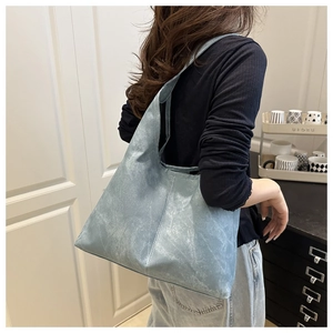 Side view of large light blue suede tote bag worn on shoulder in a minimalist room