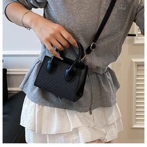 Dettaglio mini tote bag nera con strisce verticali e finiture dorate su una modella