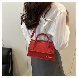 Detail view of red crocodile pattern handbag worn by model against white shirt