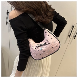 Detail of pink bow-print crescent bag with ribbon accents and heart charm on a model