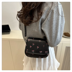 Detail of black PU leather saddle bag featuring sweet red cherry prints and slim shoulder strap