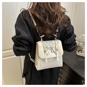 Detail of minimalist beige leather backpack featuring a bow and heart pendant on a model