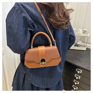 Detail of the woven texture and smooth leather finish on a brown box bag with a gold clasp