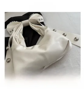 Close-up of cream white handbag with metallic rivets and decorative bow detail