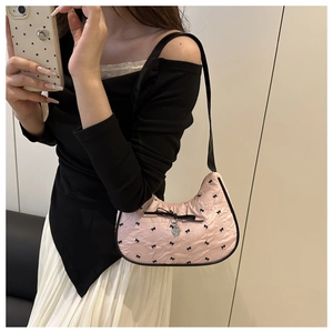 Pink shoulder bag with black bow embroidery and heart pendant detail shown on a model