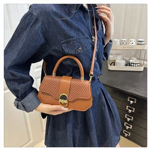 Detail of a brown textured crossbody bag with a gold metal clasp shown on a model
