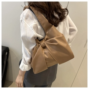 Close-up of khaki shoulder bag with large bow design on model for size reference