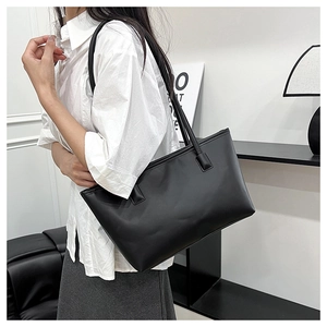 Close-up of minimalist black leather tote bag worn by a model in a modern interior setting