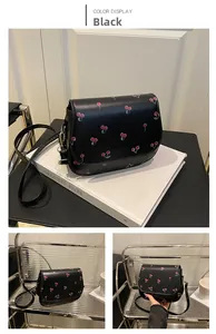 Detail view of black PU saddle bag with red cherry print and slender leather strap