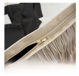 Détail de la fermeture éclair dorée et des longues franges sur un sac beige