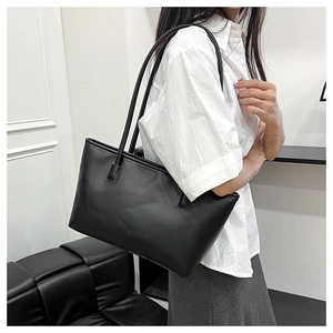 Minimalist black matte leather tote bag shown on shoulder in a modern indoor setting