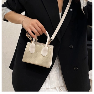 Détail du sac à bandoulière en cuir blanc et tissé beige porté avec un blazer noir