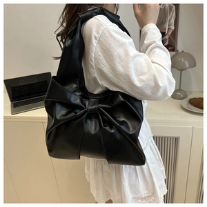Close-up of stylish black faux leather tote bag with a large decorative bow detail