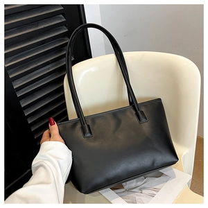 Detail of a large black tote bag in matte synthetic leather on a white chair